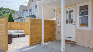 A house with a covered porch, a wooden fence, and a white door. - Cozy 2-Bedroom Home: Modern Amenities, WiFi, and AC—3 Blocks from Pier Village (Long Branch)
