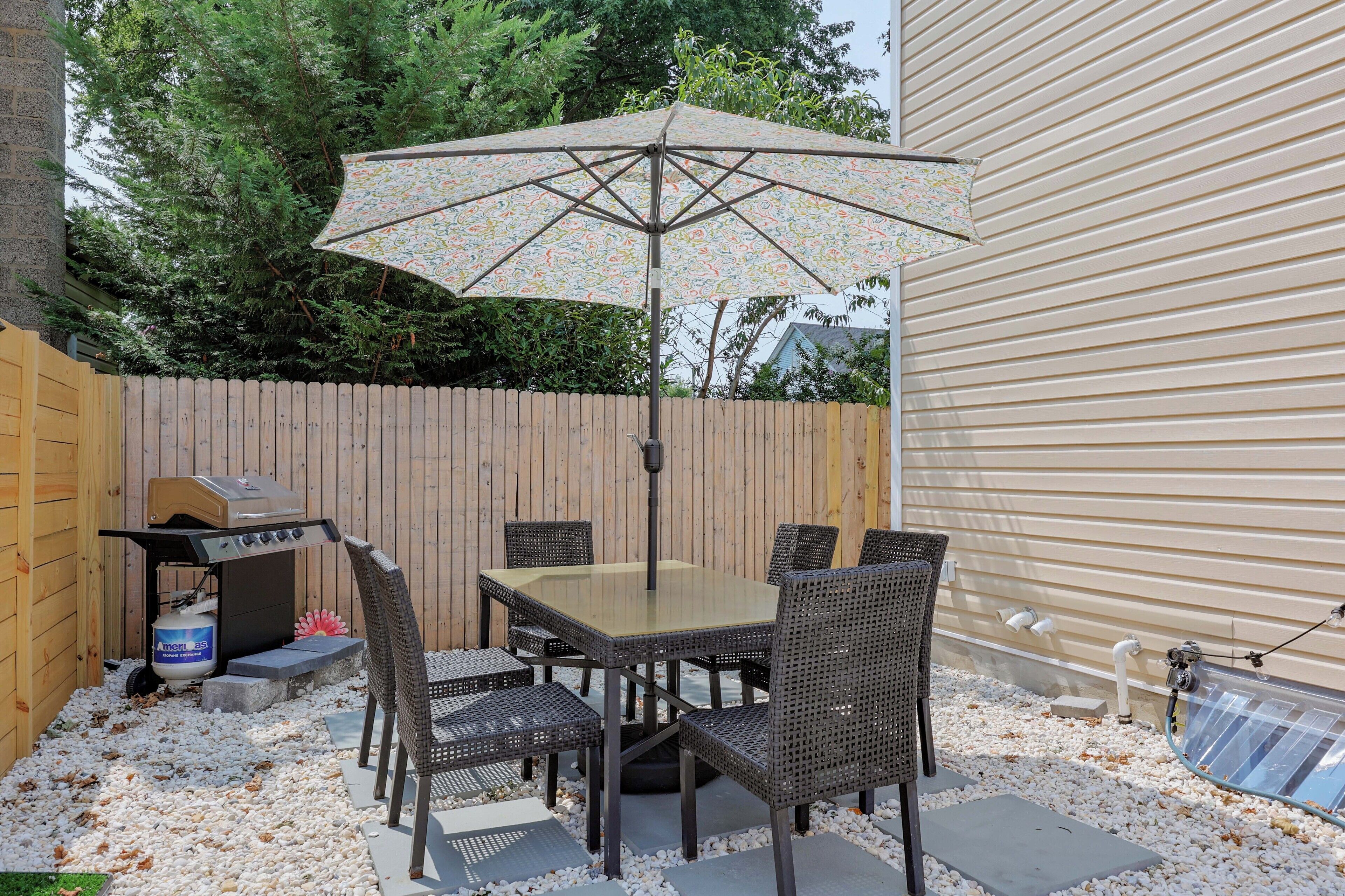 Eine Terrass mit Tisch, Stühlen, einem Grill und einem großen Sonnenschirm.
