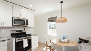 A modern kitchen with white cabinets, stainless steel appliances, and a dining area with a wooden table and chairs. - Cozy 2-Bedroom Home: Modern Amenities, WiFi, and AC—3 Blocks from Pier Village (Long Branch)