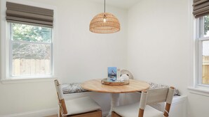 A dining area with a round wooden table, two chairs with cushioned seats, a woven pendant light, and a window with blinds. - Cozy 2-Bedroom Home: Modern Amenities, WiFi, and AC—3 Blocks from Pier Village (Long Branch)