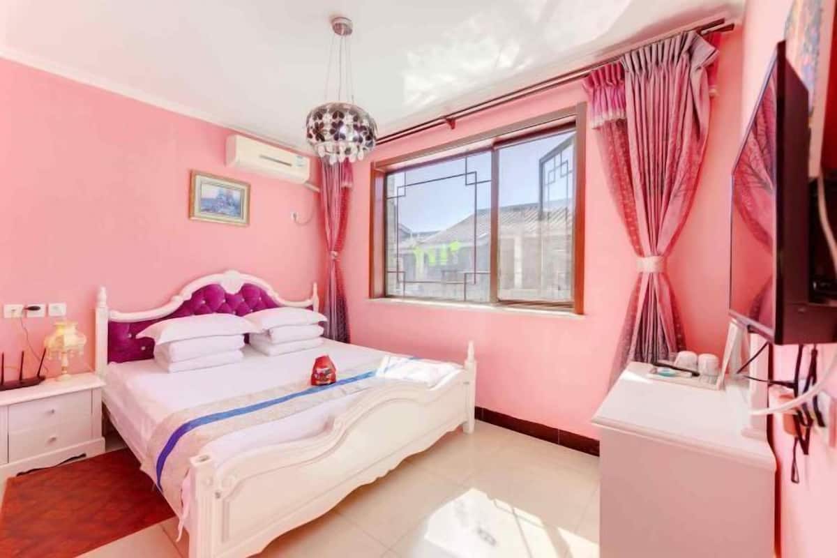 A bedroom with a bed, a nightstand, a dresser, a window with curtains, and a ceiling light fixture.