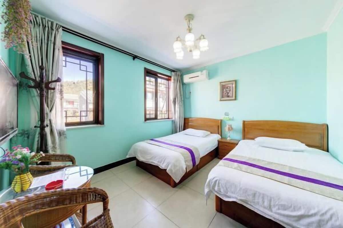 A room with two beds, a table with chairs, a window, and an air conditioning unit.