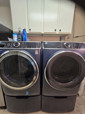 Two front-loading washing machines with control panels, a white cabinet above, and a bottle of Downy detergent on the counter. - Five Full Appointed Bedroom House in Quiet Neighborhood (Baker)
