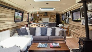 Ein gemütliches Interieur mit einer Couch, einem Couchtisch, einem Kamin und einer Küchenzeile mit Fenster und Holzwänden.