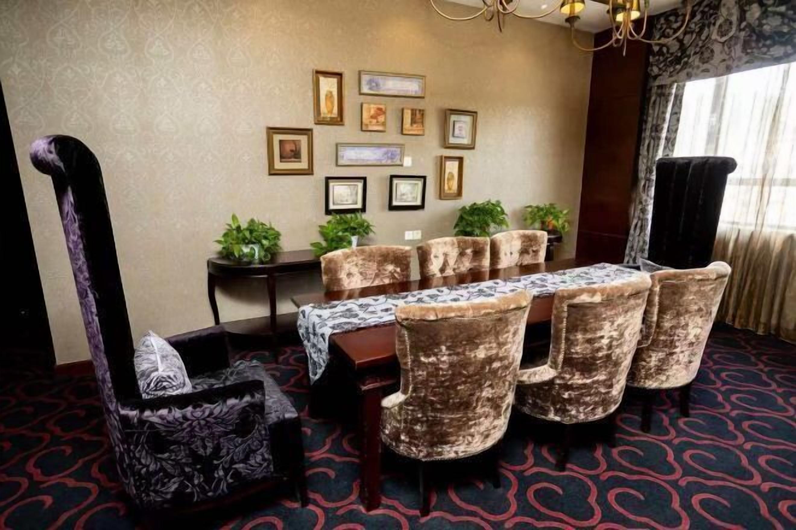 Un comedor con una mesa dispuesta para seis personas, rodeada de sillas de terciopelo, un sofá estampado y cuadros en la pared.
