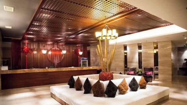 A hotel lobby with a reception desk, a seating area with a white sofa and decorative pillows, and a ceiling with a perforated design. - Rongchen International Holiday Hotel (Zhangjiakou)