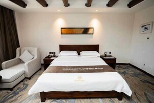A hotel room with a large bed, a chair, a nightstand, and a wall-mounted artwork.