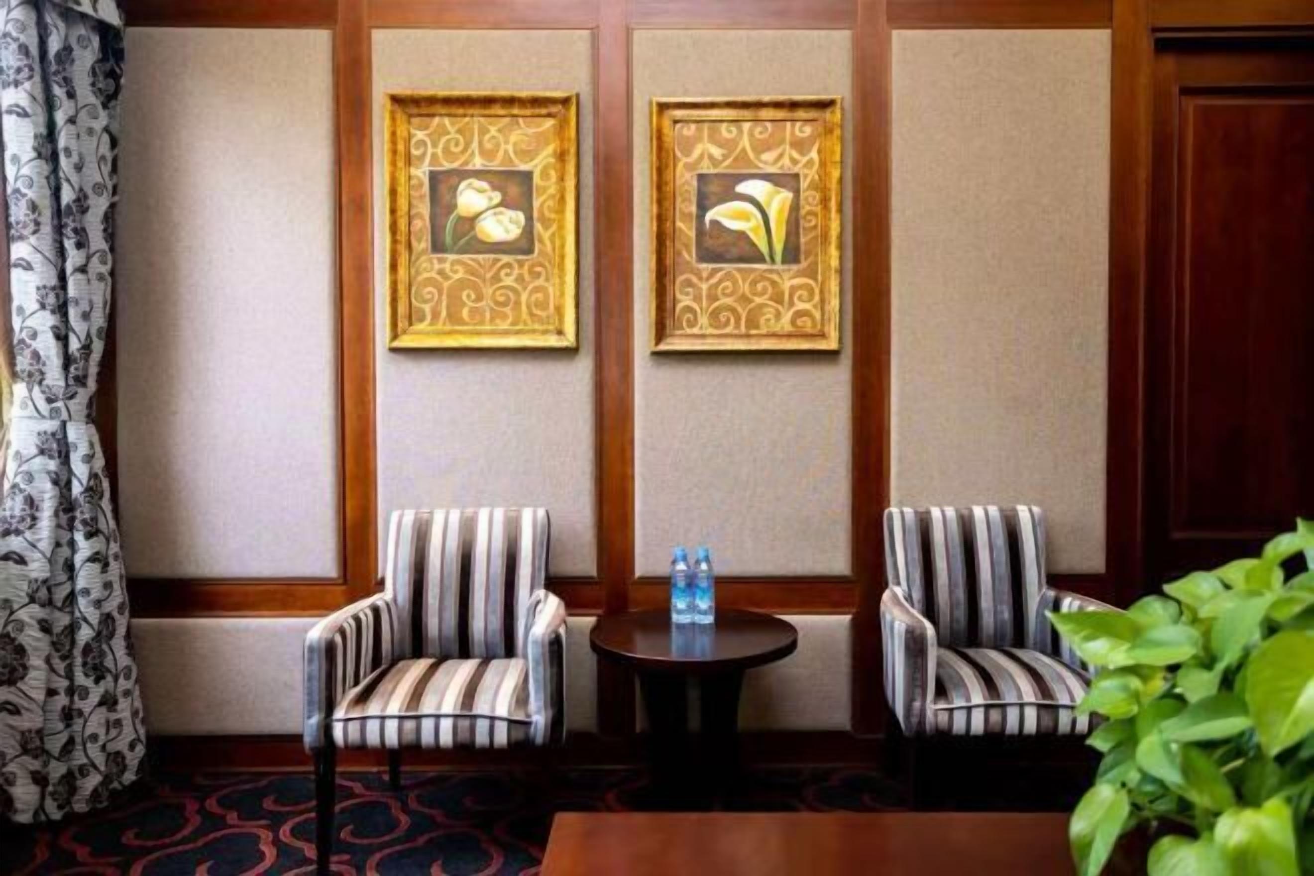 A hotel room with two striped armchairs, a small round table with a bottle, and two framed artworks on the wall.