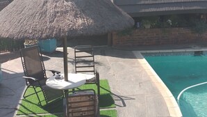Ein Poolbereich mit einem Strohdachschirm, einem Tisch und Stühlen.