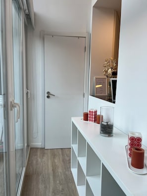 A hallway with a white door, a glass door, and a white console table with decorative items. - Burgães II Apartment (Porto)