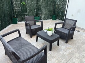 A patio area with wicker furniture, including two chairs and a table, and a potted plant. - Burgães II Apartment (Porto)