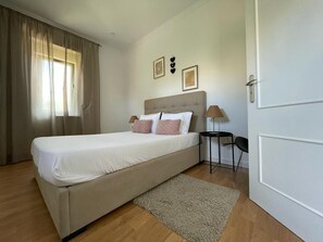 A bedroom with a bed, a nightstand, a lamp, and a door. - Burgães II Apartment (Porto)