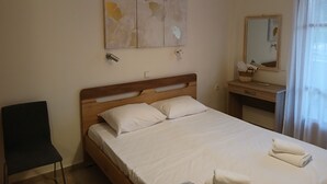 A neatly made bed with white linens and pillows, a wooden headboard, a bedside table with a lamp, a wall-mounted air conditioner, and a large abstract painting above the bed. - TOLO BLUE BAY (Nafplio)