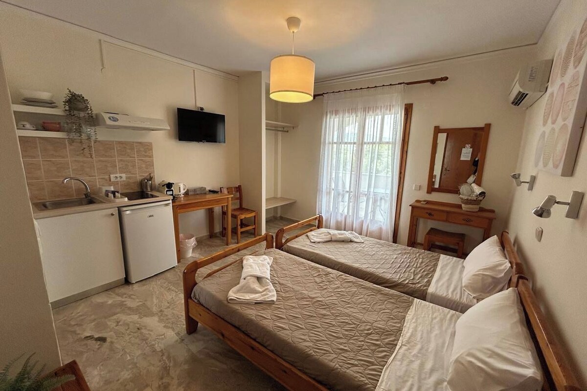 A hotel room with two beds, a kitchenette, a television, and a window with curtains.