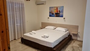 A neatly made bed with white linens and two pillows, a wooden headboard, and a painting of a sailboat on the wall. - TOLO BLUE BAY (Nafplio)