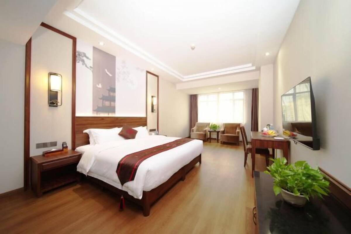 Una habitación de hotel con cama, mesitas de noche, escritorio, silla, televisor y una planta.