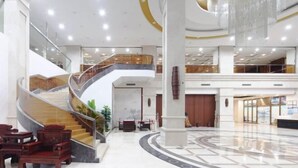 A spacious lobby with a curved staircase, a reception desk, and a seating area with wooden chairs. - Yunding International Hotel (Sanjiang)