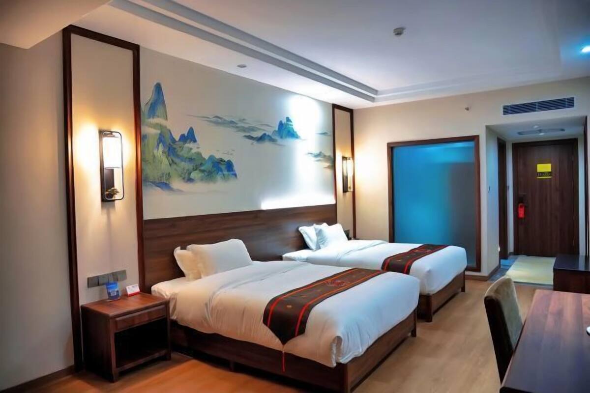Habitación de hotel con dos camas, cabecera de madera, un cuadro de montañas y un escritorio con silla.
