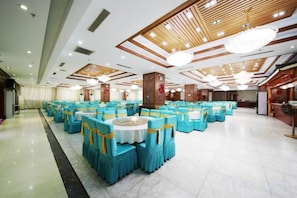 Un salón de banquetes con mesas y sillas redondas, paneles de techo de madera y candelabros.