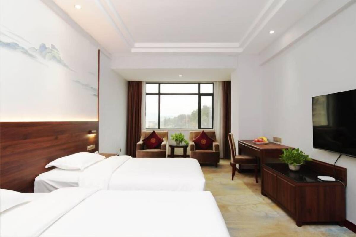 Habitación de hotel con dos camas, un escritorio, una silla, un televisor y una ventana con cortinas.