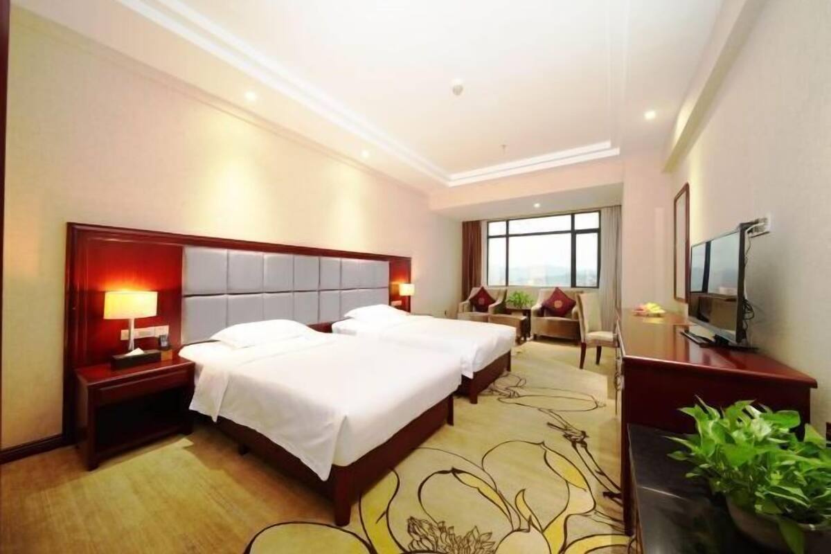 Habitación de hotel con dos camas, televisor, escritorio y ventana grande.