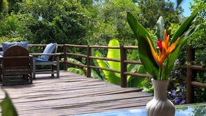 A wooden deck with a glass table and a chair with a blue cushion. - Villa Nobre Trancoso (Porto Seguro)