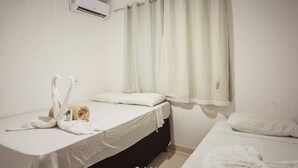 A room with two beds, a window with curtains, an air conditioning unit, and towels on the beds. - Villa Nobre Trancoso (Porto Seguro)