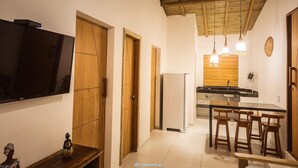 A modern kitchen with a flat-screen TV, wooden doors, a refrigerator, and a dining area with stools. - Villa Nobre Trancoso (Porto Seguro)