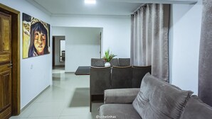 A modern living room with a grey sofa, a dining area with a table and chairs, and a painting on the wall. - Villa Nobre Trancoso (Porto Seguro)