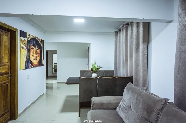A modern living room with a grey sofa, a dining area with a table and chairs, and a painting on the wall. - Villa Nobre Trancoso (Porto Seguro)
