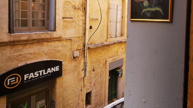 A narrow urban street with buildings, a sign for 'FASTLANE', and a framed artwork on a wall.
