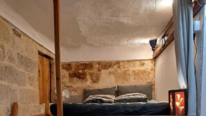 A loft bedroom with a wooden ladder, a bunk bed, and a rustic stone wall.