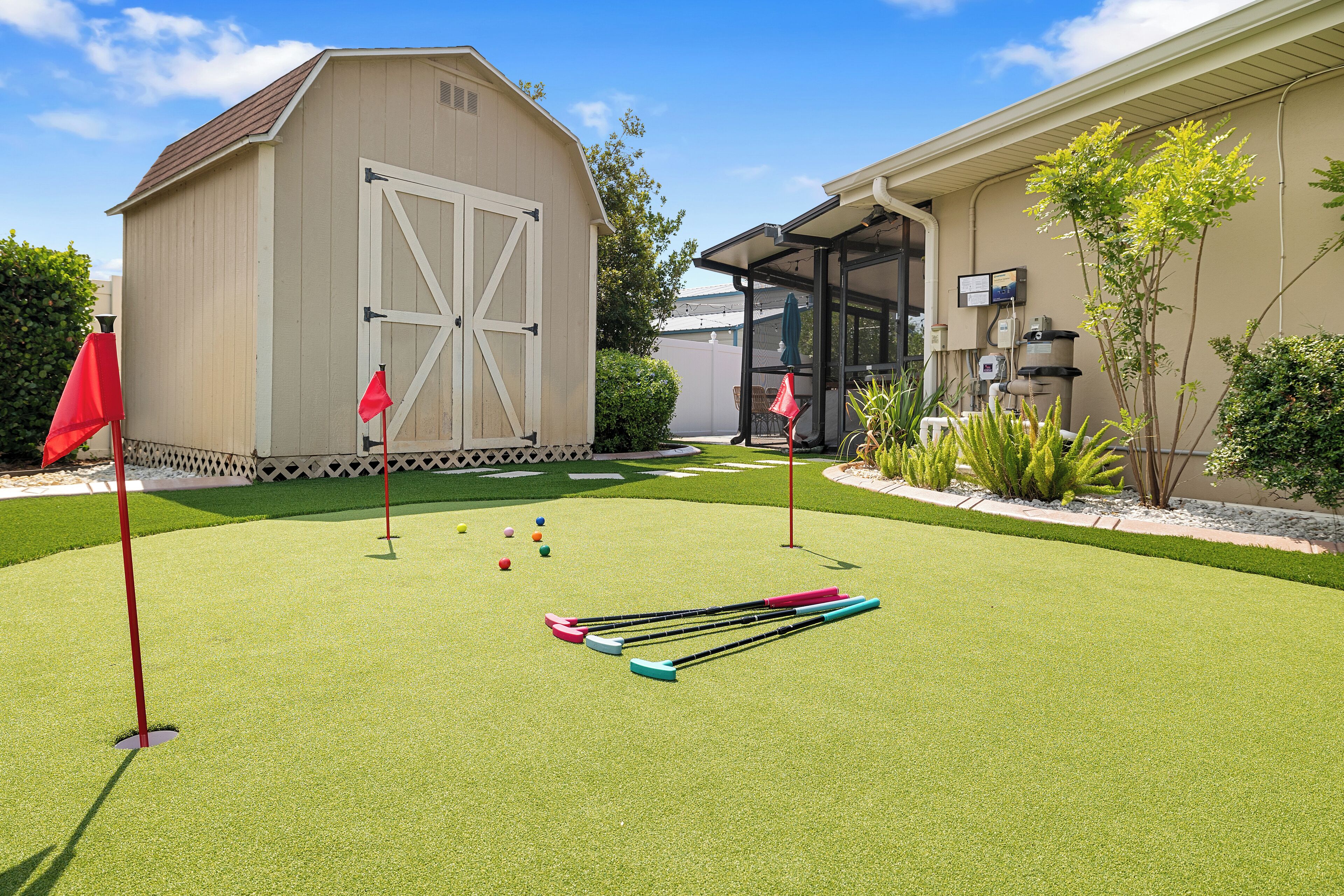 A well-maintained artificial grass lawn with a croquet set and a shed in the background.