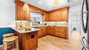 A kitchen with wooden cabinets, a granite countertop, and a large island with stools. - Palm Paradise Retreat - Heated Pool, Spa, Mini Golf (Seminole)