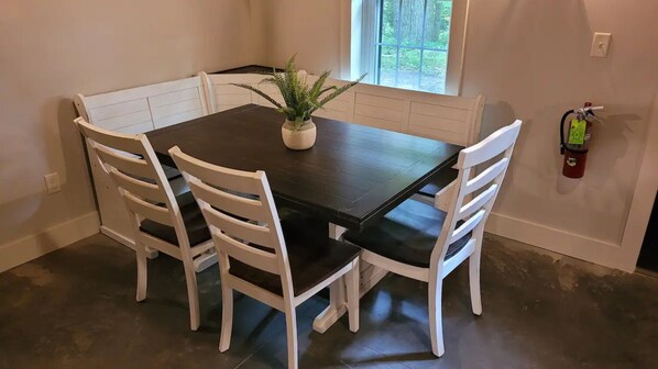 A dining table with four white chairs, a potted plant, and a fire extinguisher on the wall.