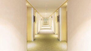 Un largo y estrecho pasillo de hotel con alfombra estampada, paredes de colores claros y puertas distribuidas uniformemente.