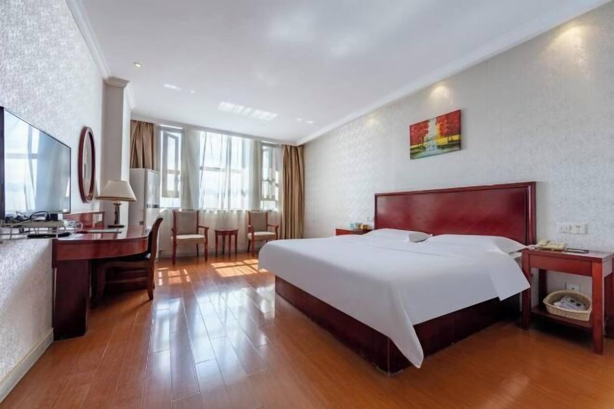 A hotel room with a large bed, a desk with a chair, a television, and a painting on the wall.