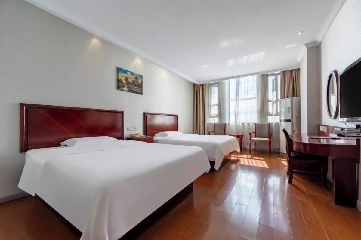 A hotel room with two beds, a desk, a chair, a TV, and a window with curtains.