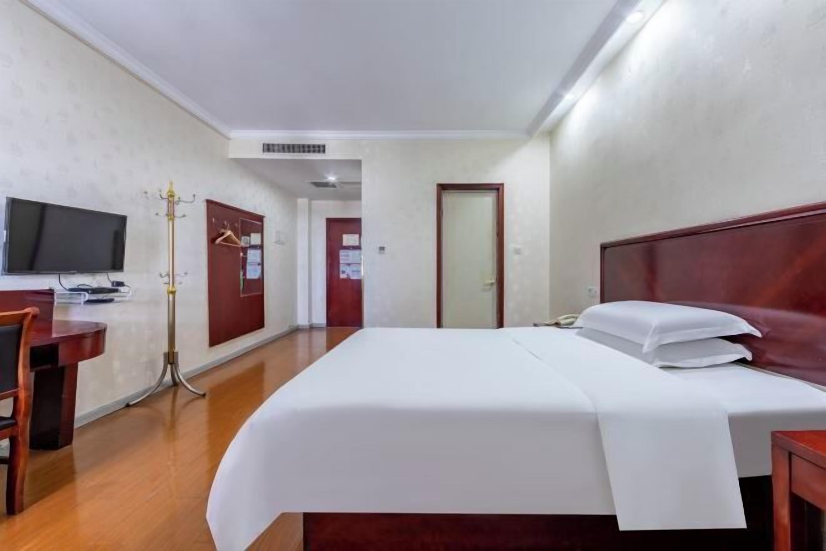 A hotel room with a bed, a desk, a chair, a television, and a coat rack.