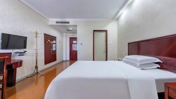 A hotel room with a bed, a desk, a chair, a television, and a coat rack.