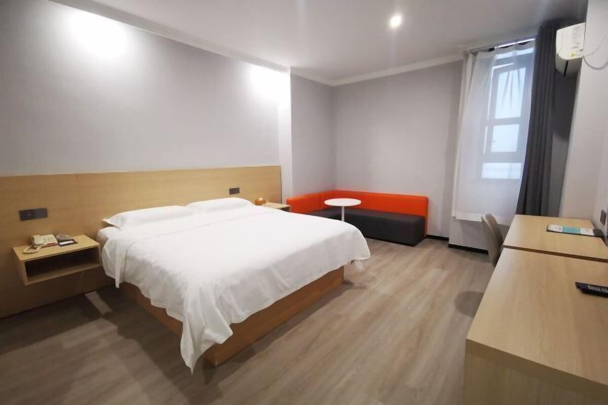 A hotel room with a bed, bedside table, a small table with a chair, a sofa, and a desk with a chair.
