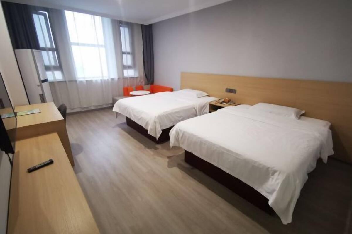 A hotel room with two beds, a desk, a chair, and a TV.