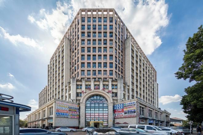 Un edificio alto de varios pisos con una entrada central en arco y un amplio frente de cristal.