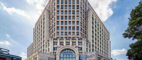 Um edifício alto, com vários andares, entrada central em arco e fachada envidraçada.