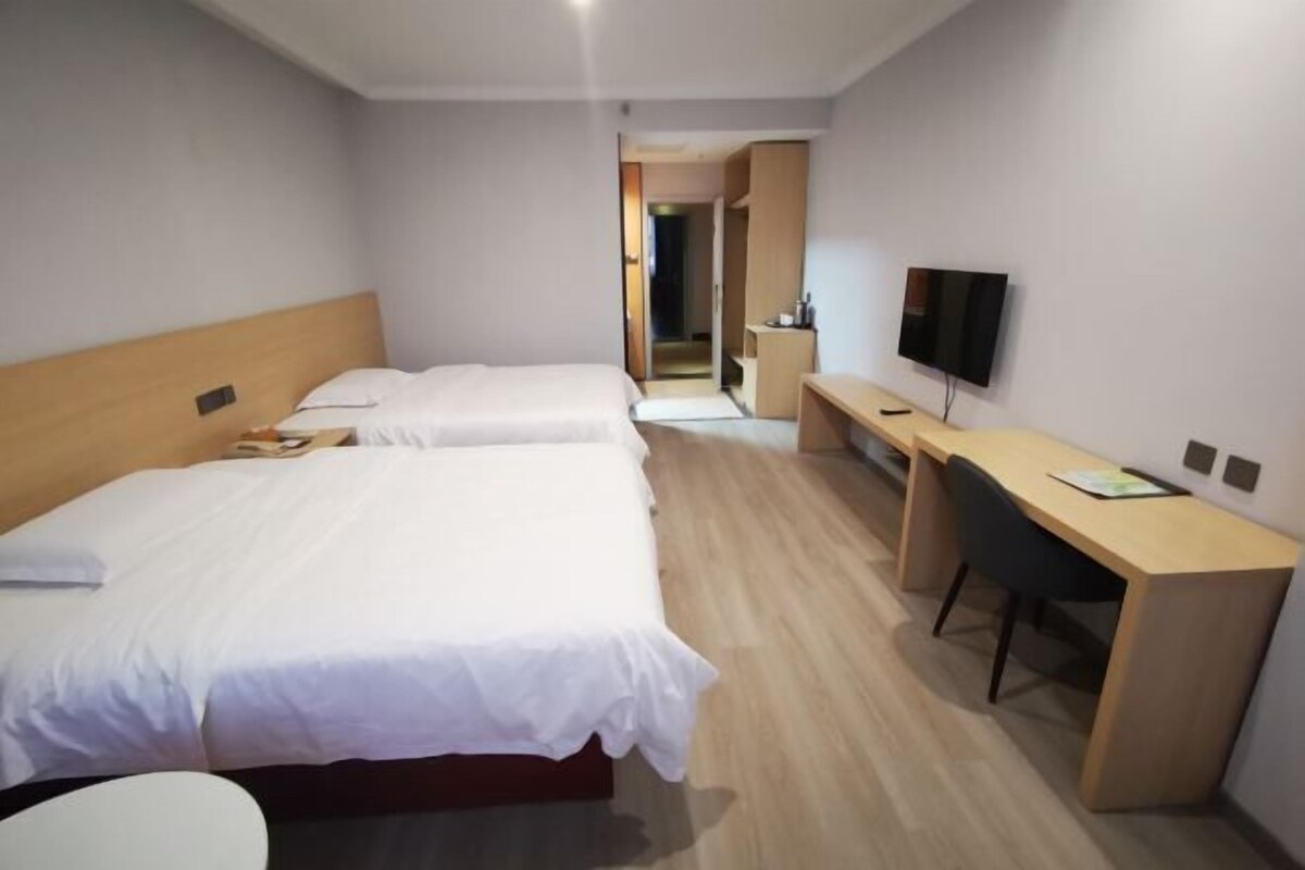 A hotel room with two beds, a desk, a chair, a TV, and a walk-in closet.