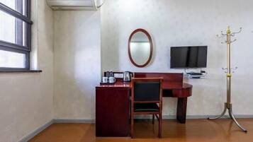 Habitación de hotel con escritorio, silla, televisor y perchero.