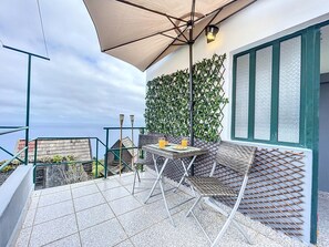 Um terraço com mesa e cadeiras, um grande guarda-sol e vista para o mar.