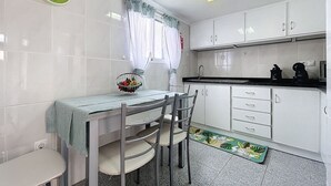 Una cocina con armarios blancos, una mesa de comedor con sillas, un frutero y un reloj en la pared.