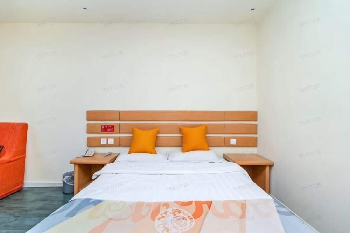Une chambre d’hôtel avec un lit, deux tables de chevet, une tête de lit en bois et une chaise orange.