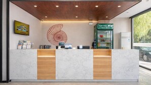 A reception area with a marble counter, wooden paneling, a large decorative wall piece, a digital screen, and a vending machine. - Shell Hotel (Chengyang Agricultural University Subway Station) (Qingdao)